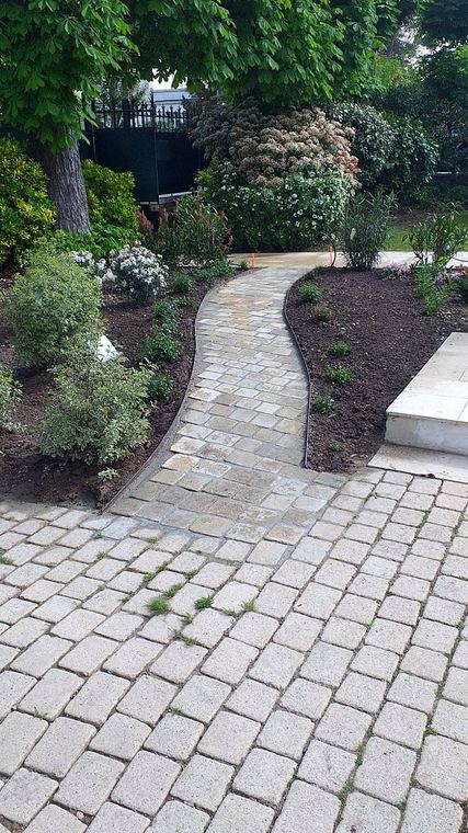Allée courbe en pavés bordée de massifs plantés